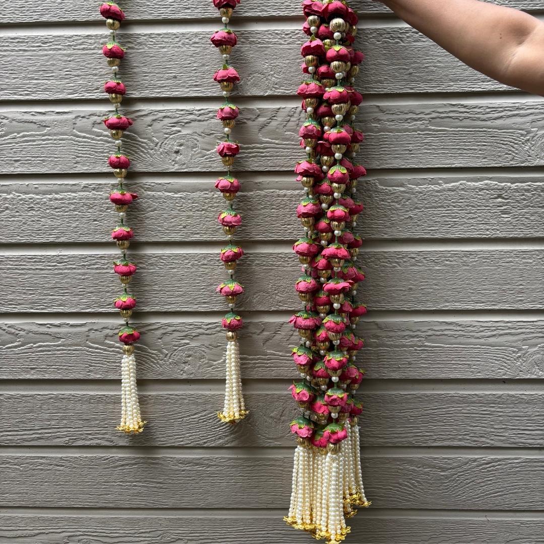 Decorative garlands with pink flowers and white beads against a gray wooden background