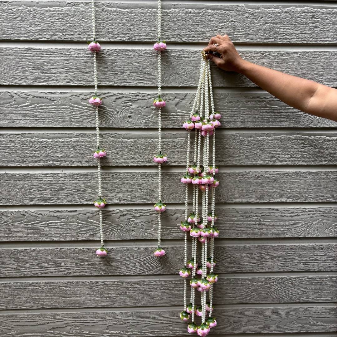 Decorative string with pink flowers being hung on a gray wall.