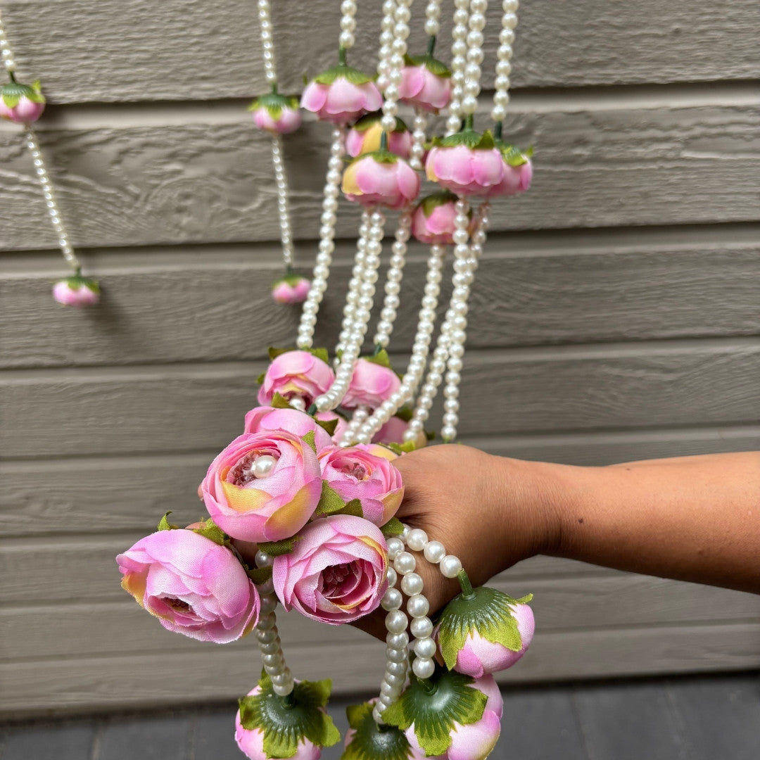 Hand holding a decorative item with pink flowers and pearls against a wooden background