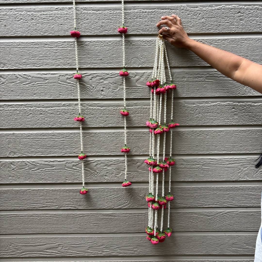 Person hanging a decorative string with pink flowers on a gray wall.