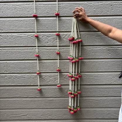 Person hanging a decorative string with pink flowers on a gray wall.
