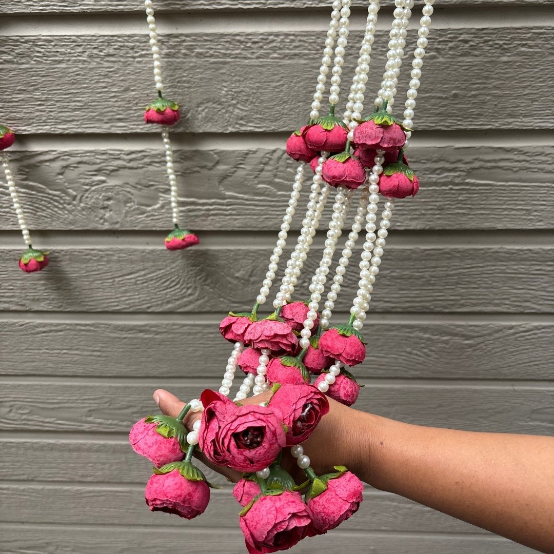 Decorative hanging with pink flowers and white beads against a wooden background