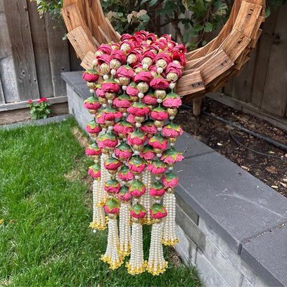 Decorative hanging garlands with red and gold flowers on a grassy area with a wooden structure in the background.