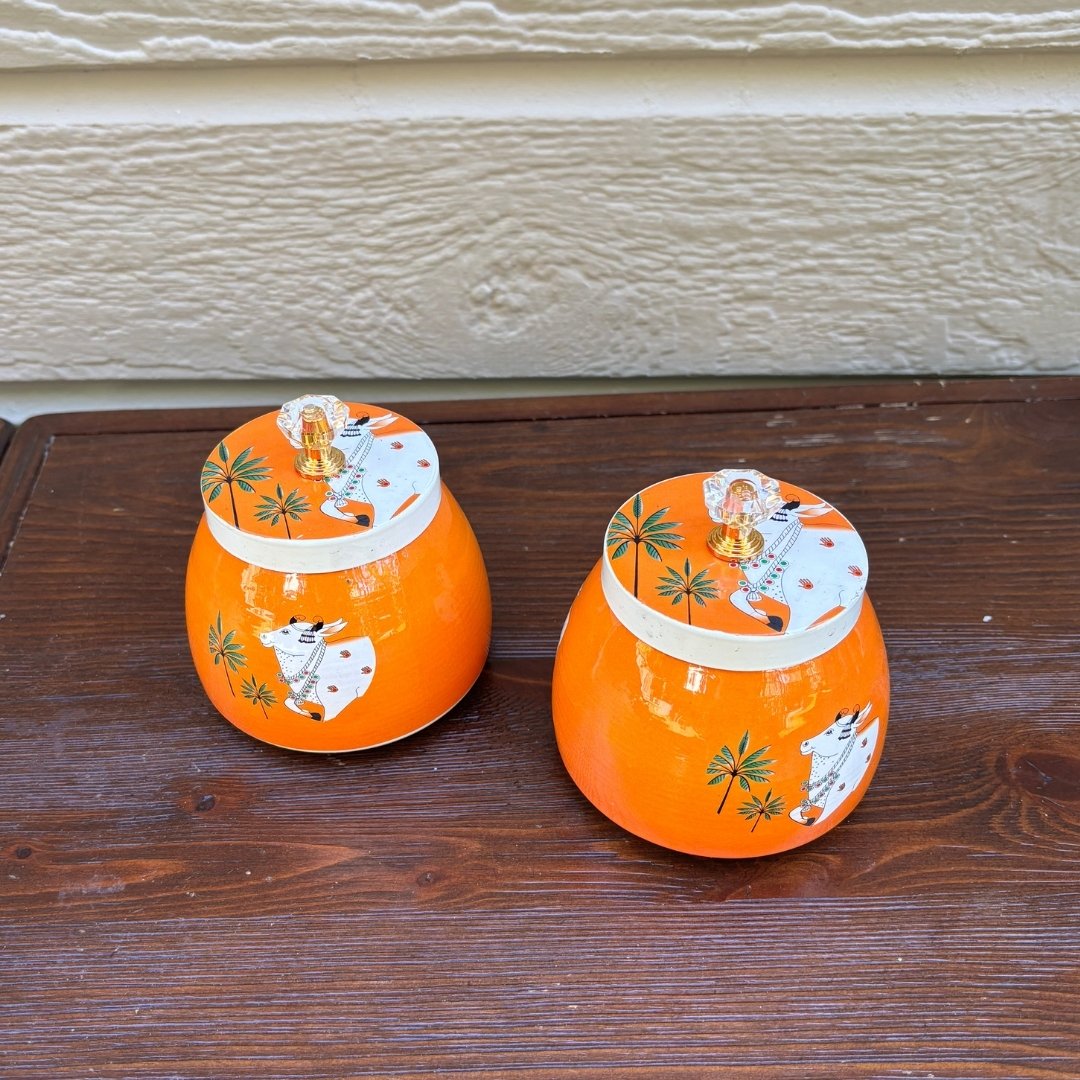Two orange metala indian jars with lids on a wooden surface.