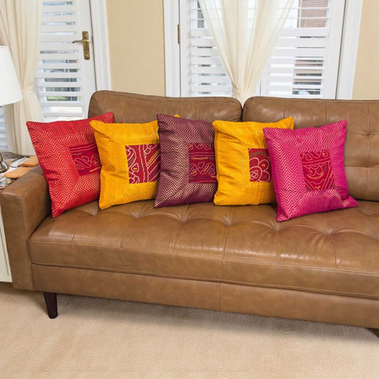 Set of 5 16×16 Bandhani silk brocade cushion covers on brown leather sofa — Diwali decor, handcrafted.
