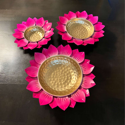 Three pink flower-shaped candle holders urli bowls with gold centers on a dark surface