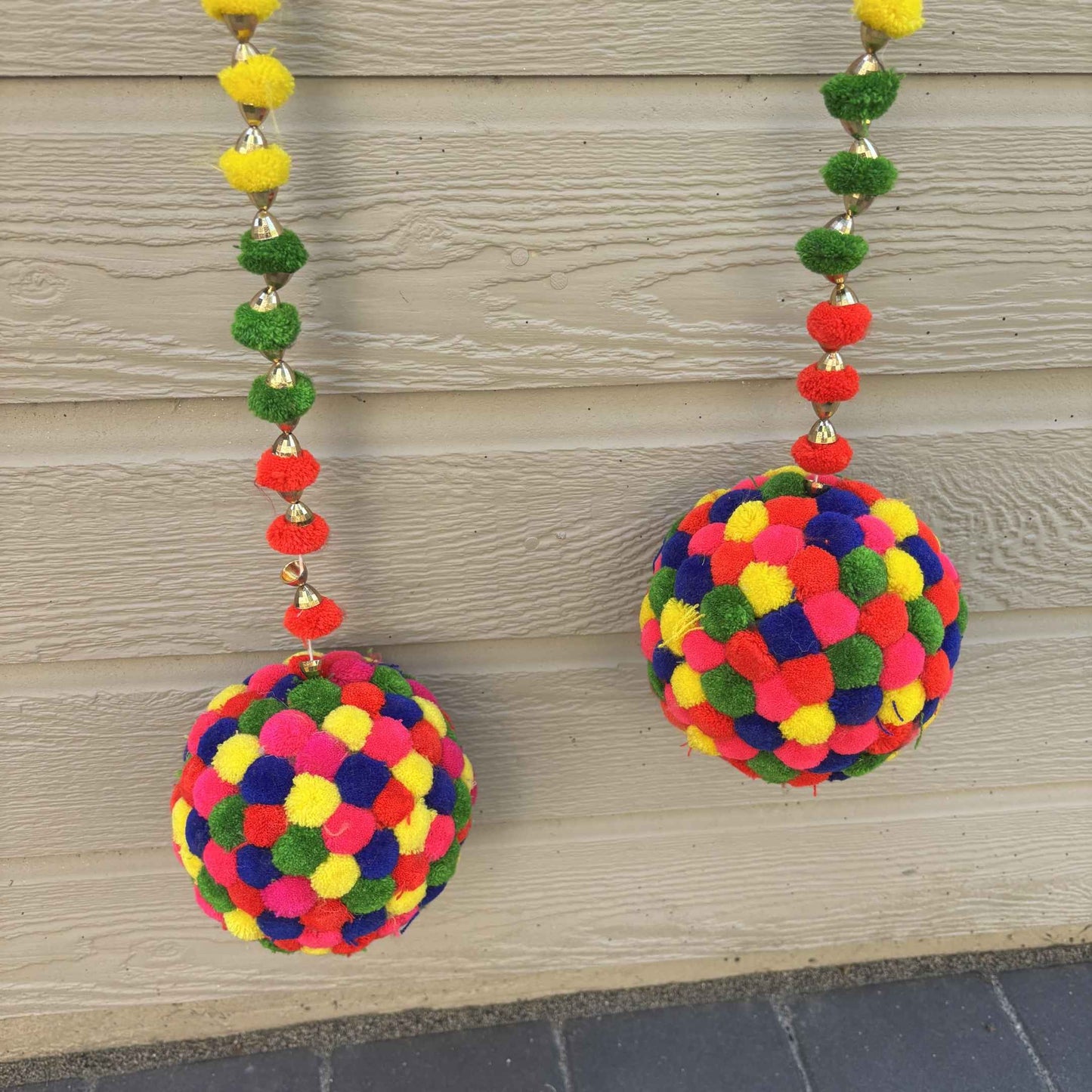 Two colorful pom-pom garlands hanging against a beige wood-paneled wall.