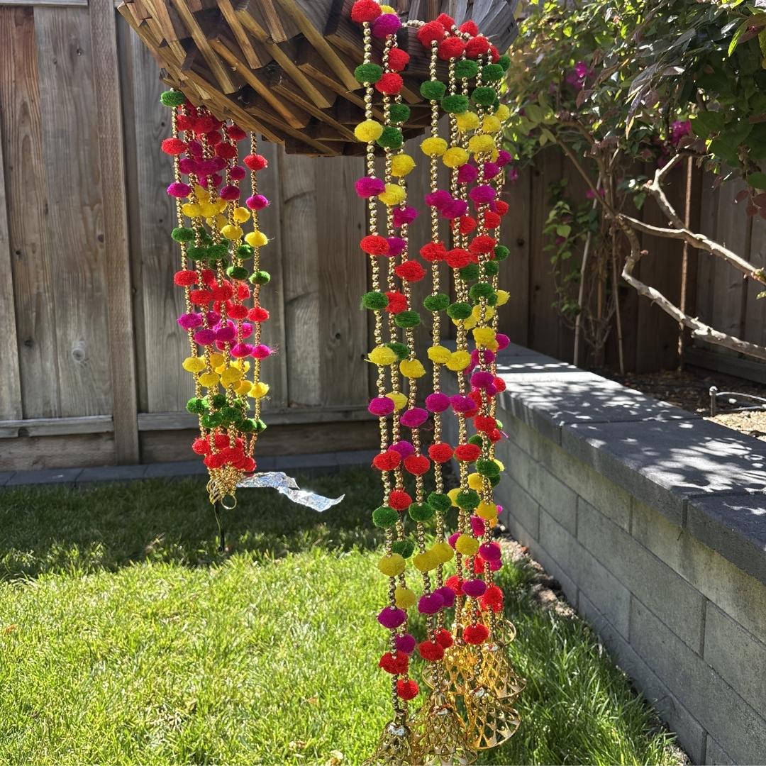Colorful pom-pom garlands hanging outdoors on a wooden pergola.