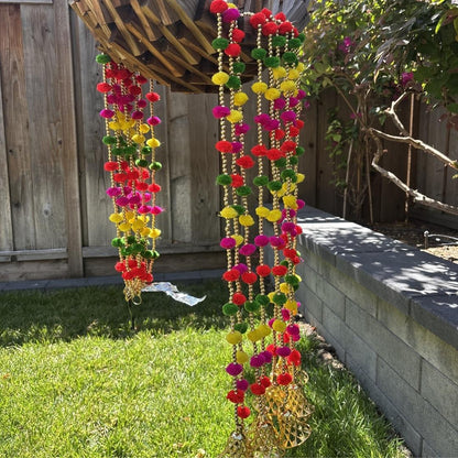Colorful pom-pom garlands hanging outdoors on a wooden pergola.