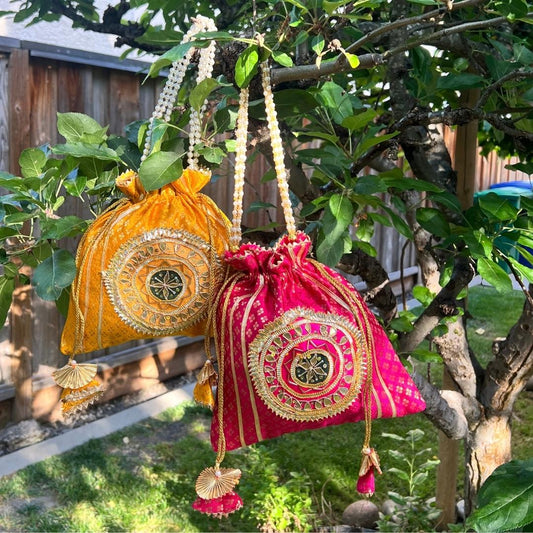 Two decorative bags, one yellow and one pink, hanging from a tree branch.
