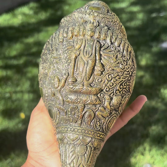 Hand rotating the hand-engraved brass Dashavatar shankh to show the carved Vishnu figure, the row of avatar faces and the medallion detail