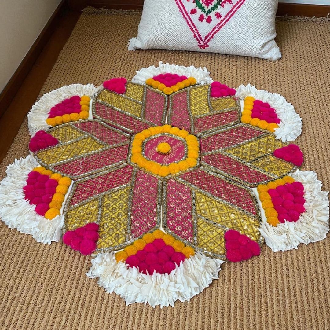 Colorful rangoli mat a brown floor with a decorative pillow in the background
