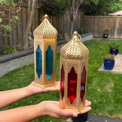 Person holding a Moroccan tealight lantern with blue stained glass and gold metal filigree, demonstrating its portability and design.