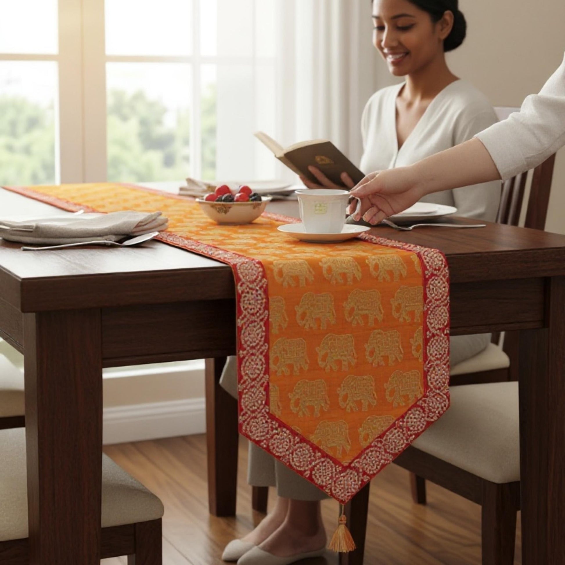 Woman sitting at a dining table with an orange table runner featuring elephant patterns.