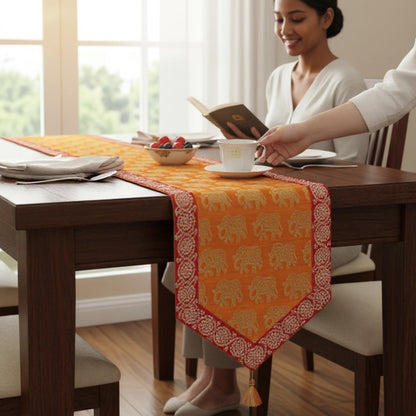 Woman sitting at a dining table with an orange table runner featuring elephant patterns.