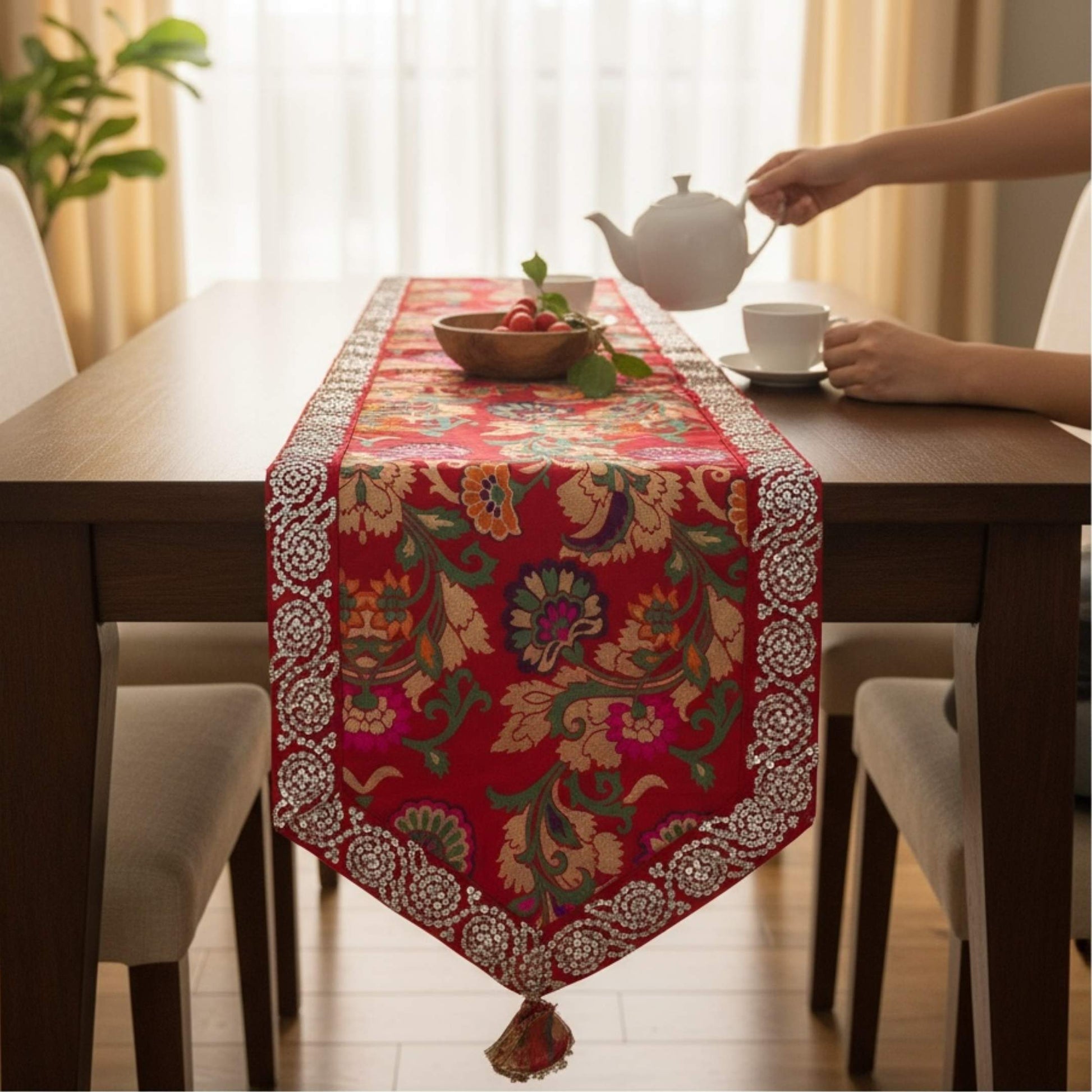 Dining table with a decorative red table runner, teapot, and cup.