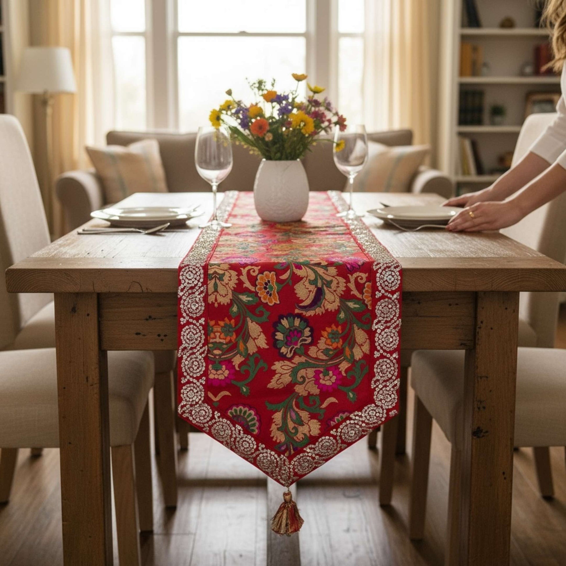 Dining table with a colorful floral table runner, flowers, and wine glasses in a cozy room.