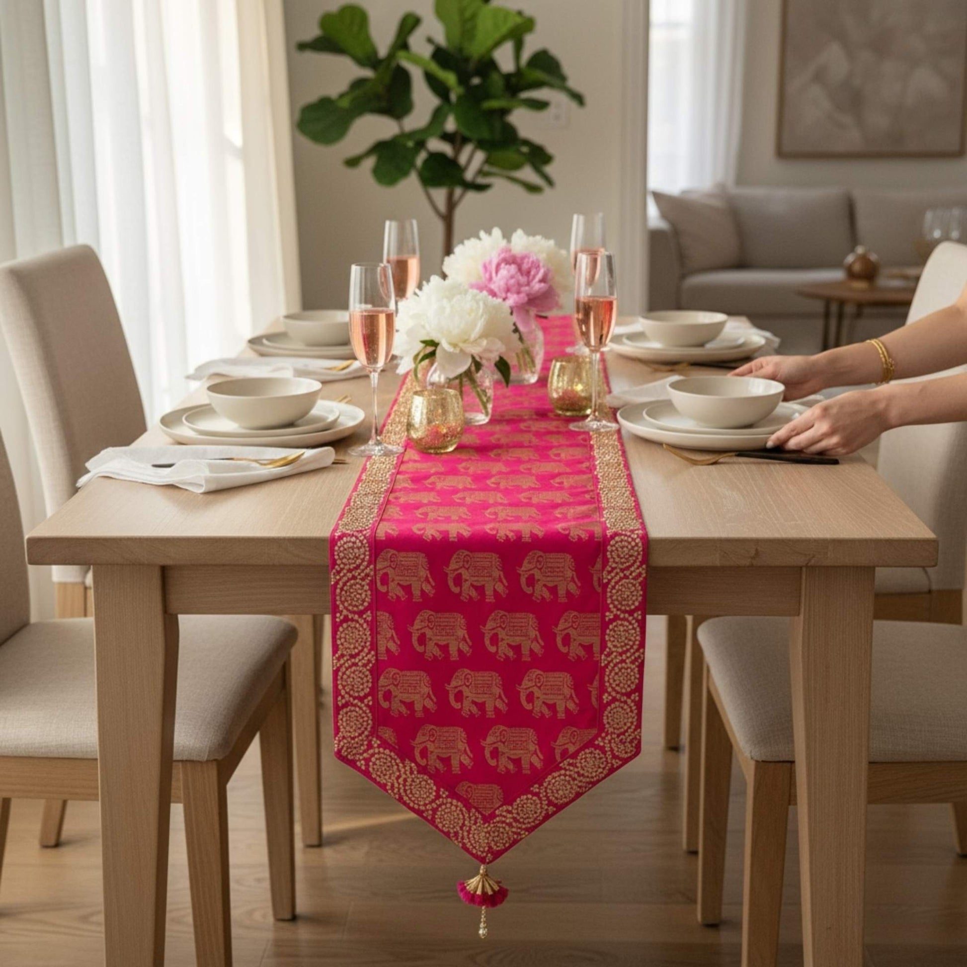 Dining table set with a pink table runner featuring gold elephant patterns, in a bright room.