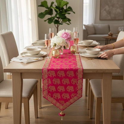 Dining table set with a pink table runner featuring gold elephant patterns, in a bright room.