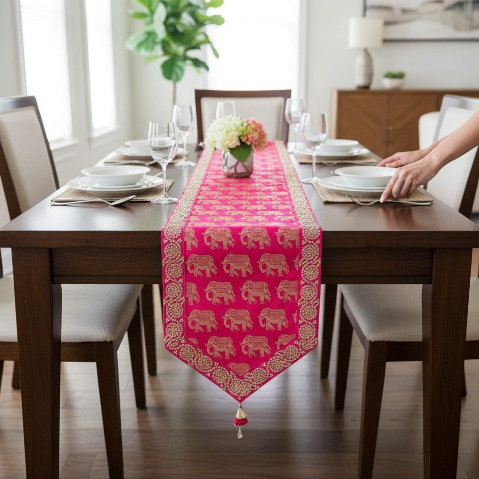 Dining table set with a pink table runner featuring gold elephants, in a bright room.