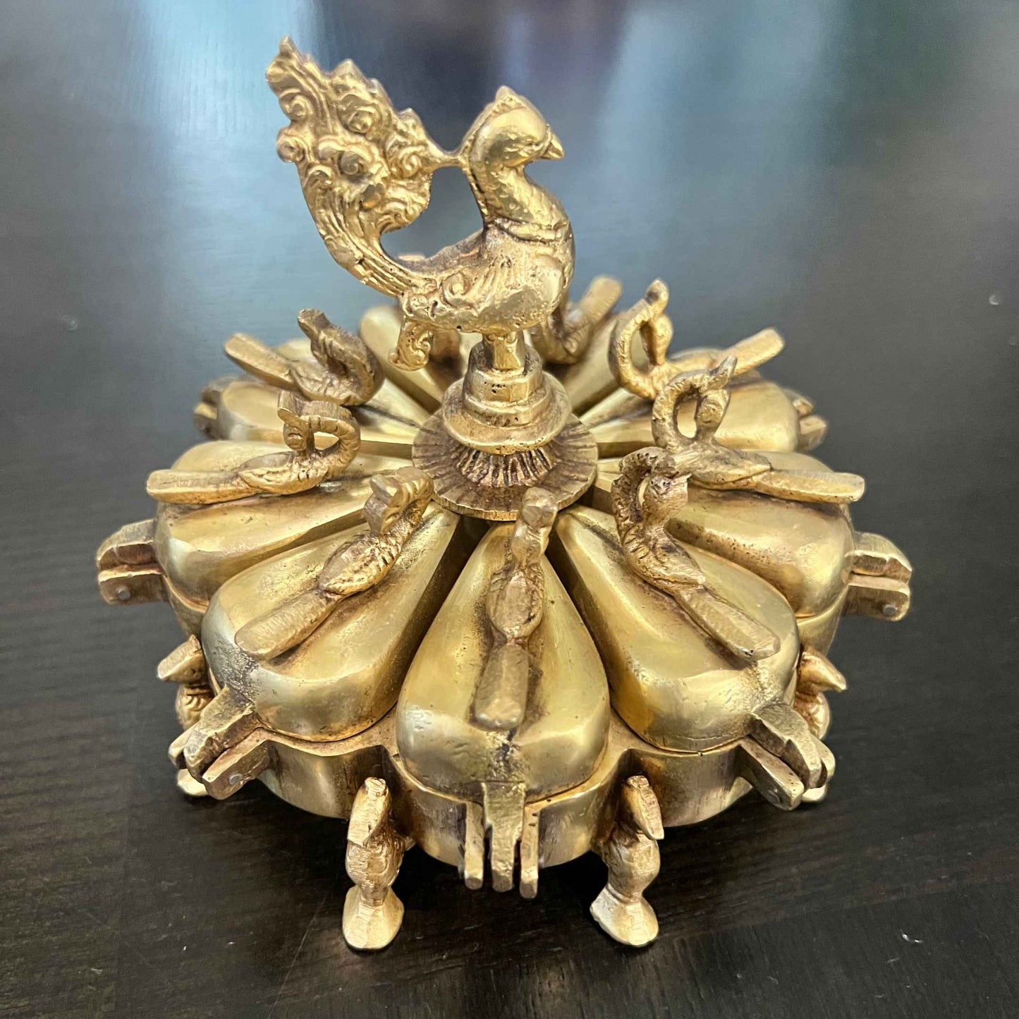 Brass Peacock Shingardani kumkum box, antique gold 9-compartment, closed view on dark wood
