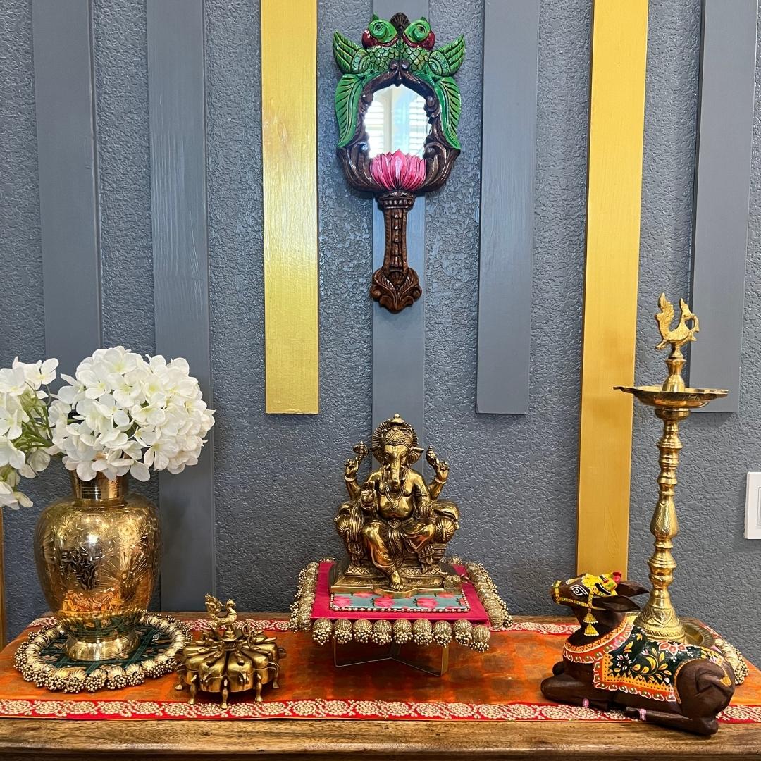 Brass kumkum box on pooja mandir display with Ganesha statue, oil lamp, and white flowers