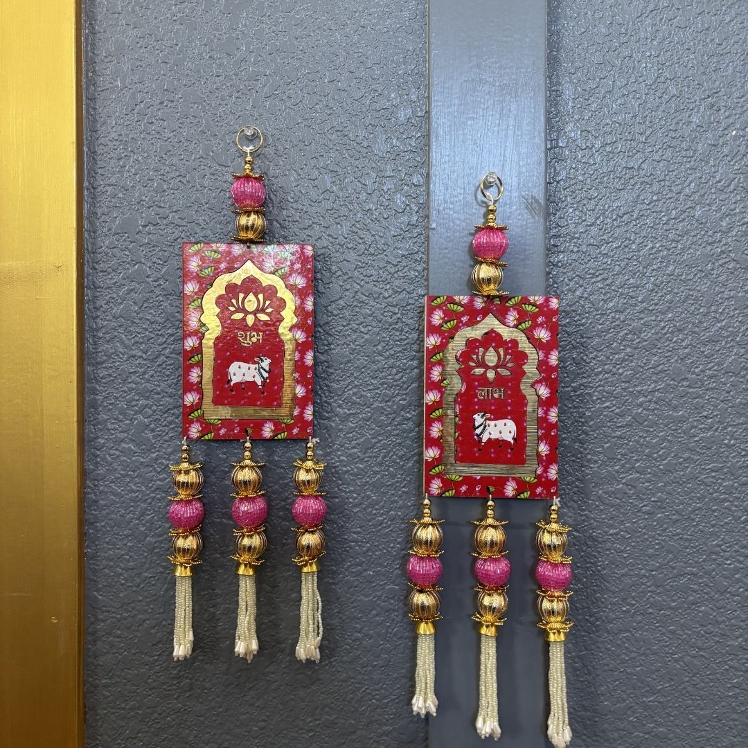 Decorative red Shubh Labh hangings with gold accents mounted on a traditional wooden door for Diwali