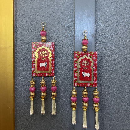 Decorative red Shubh Labh hangings with gold accents mounted on a traditional wooden door for Diwali