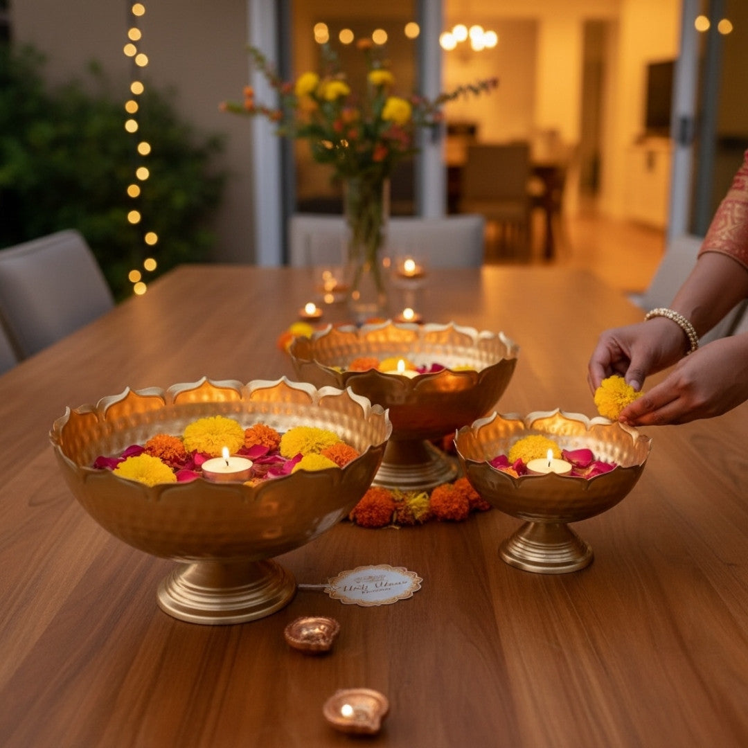 Decorative lotus urli bowls with floating flowers and candles on a wooden table, with a person's hand adding more flowers.