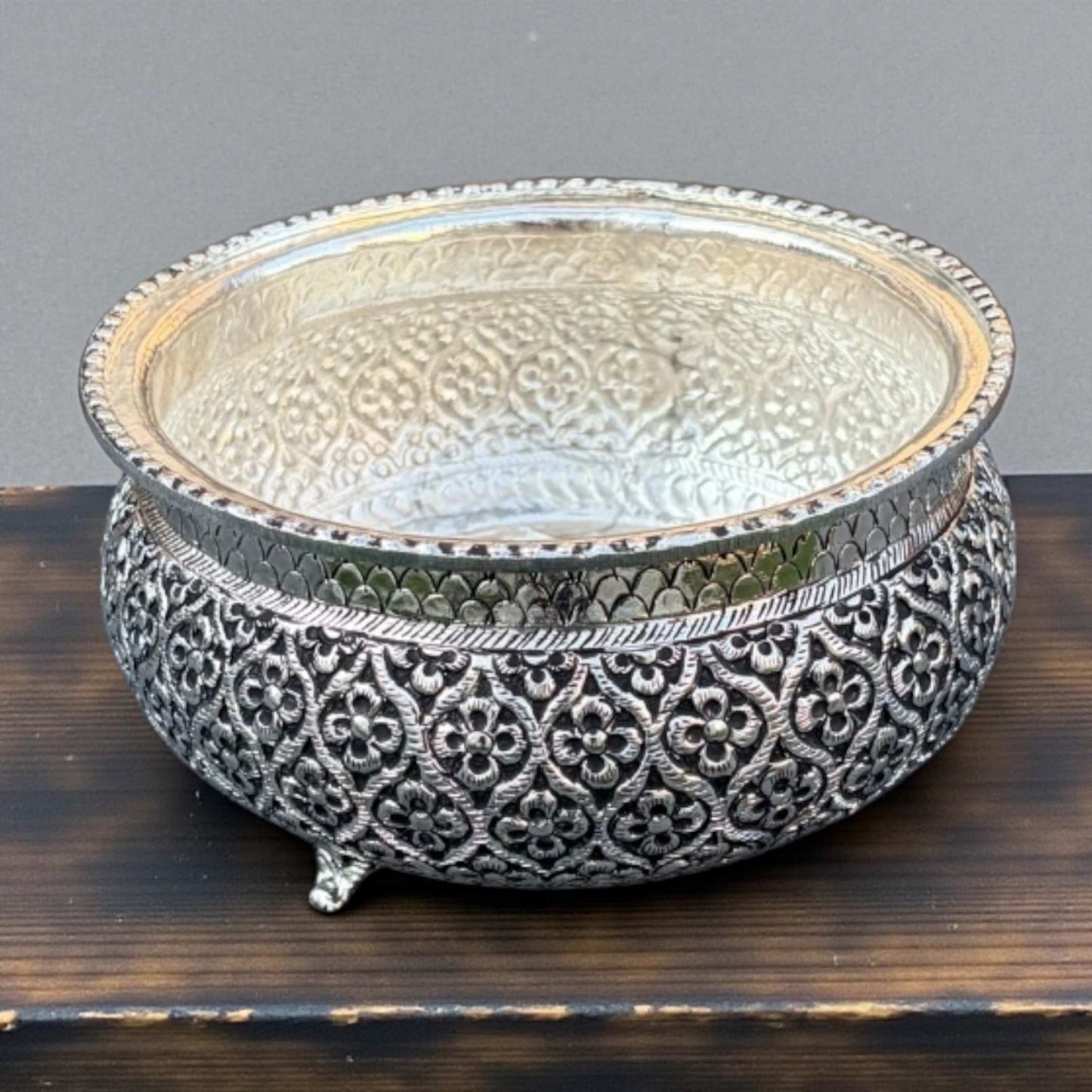 Decorative silver bowl with intricate patterns on a wooden surface.