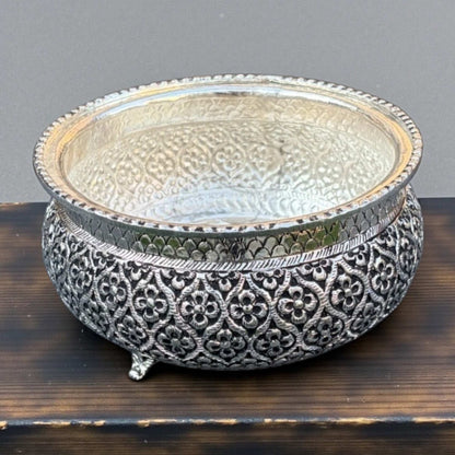 Decorative silver bowl with intricate patterns on a wooden surface.