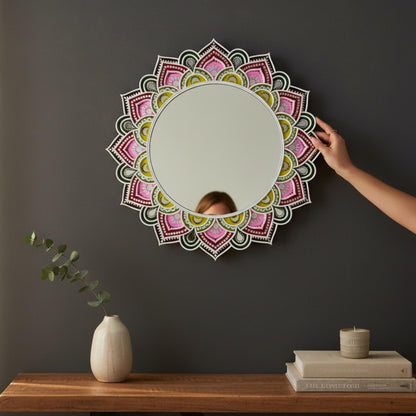 Decorative lippan mirror with mandala design on a dark wall, with a hand adjusting it.