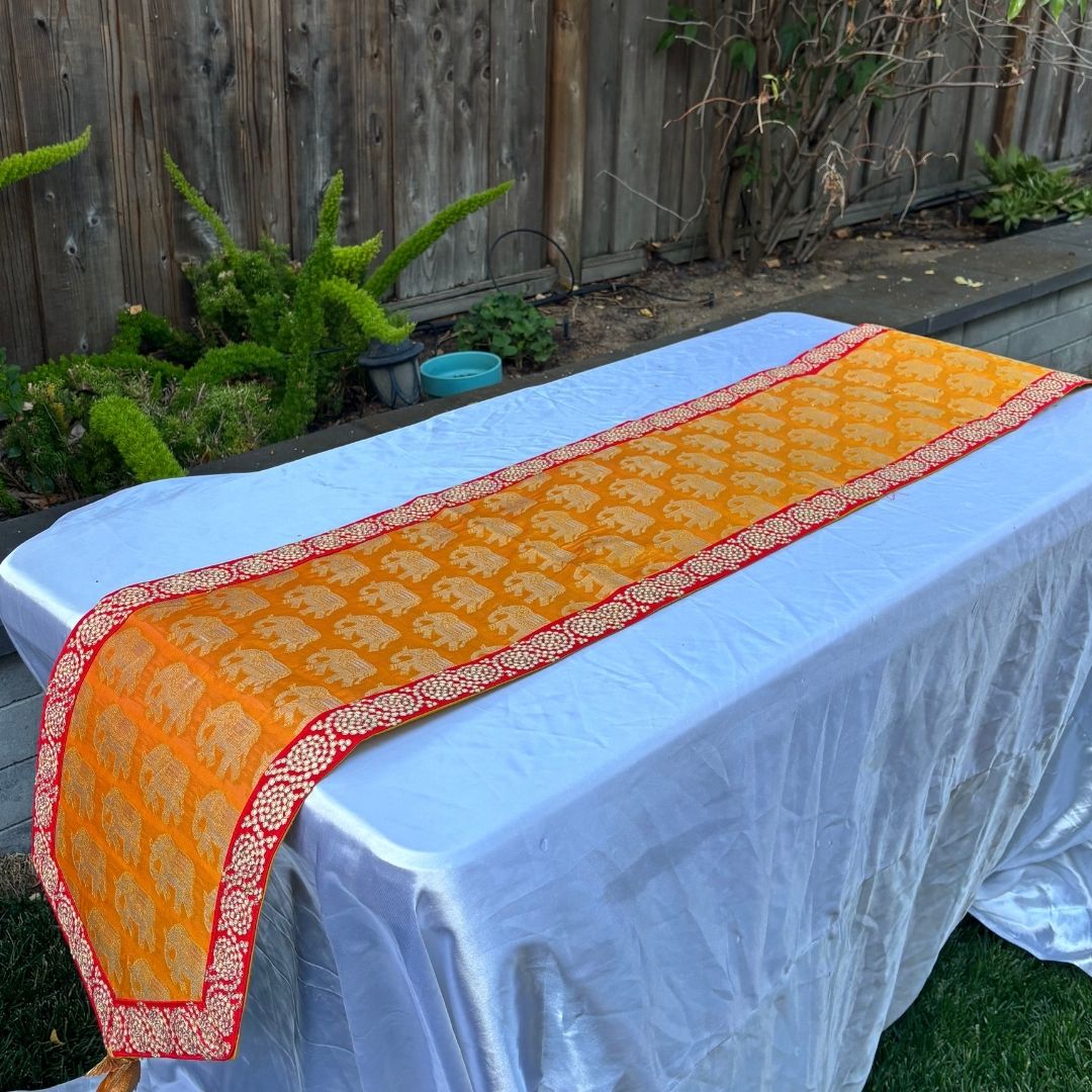 Orange and red patterned table runner on a white table outdoors.