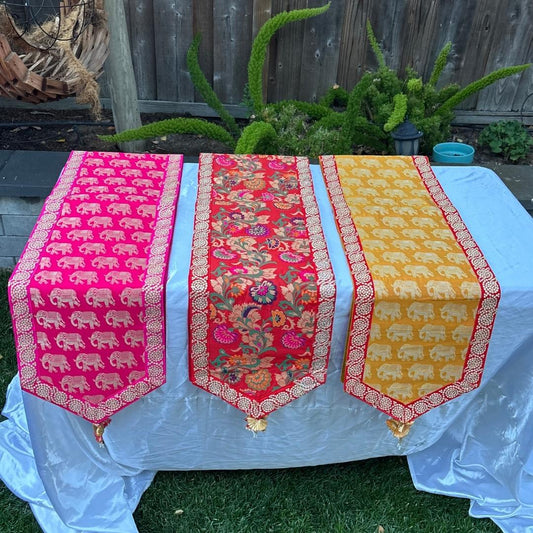 Three colorful table runners with elephant patterns on a white tablecloth outdoors.