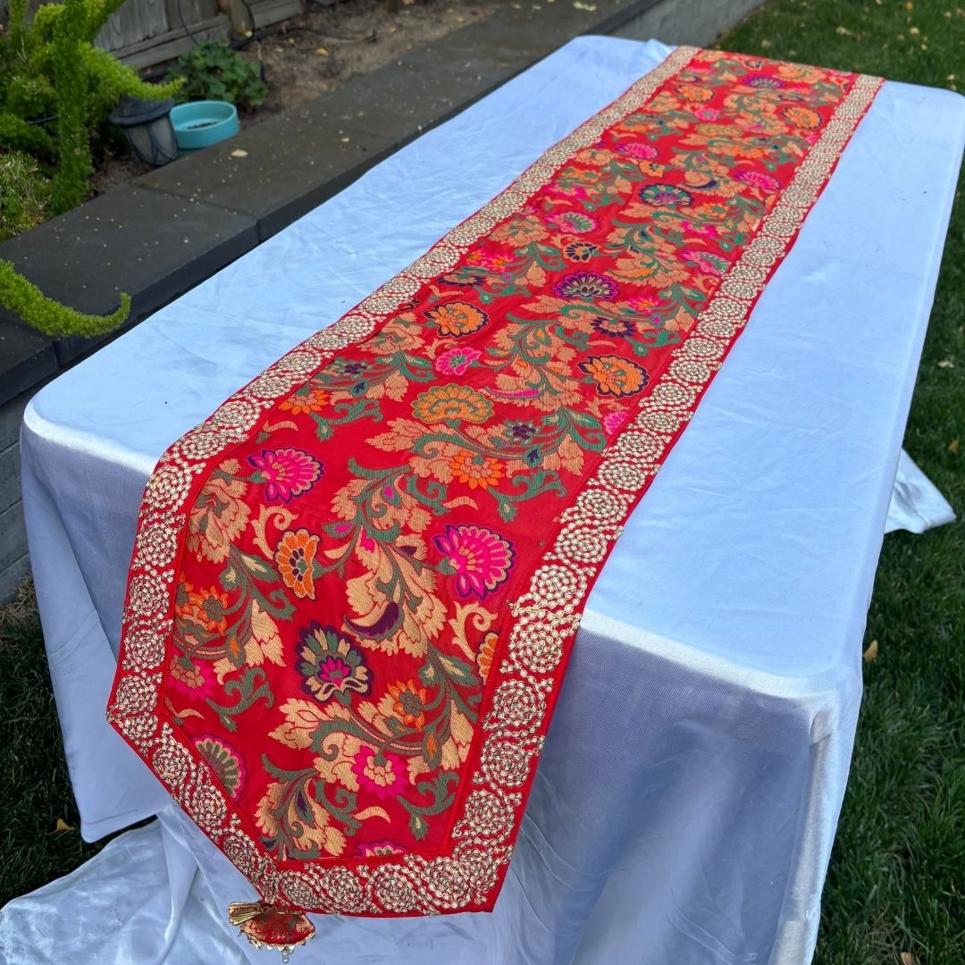 Decorative red table runner with floral patterns on a white tablecloth outdoors.