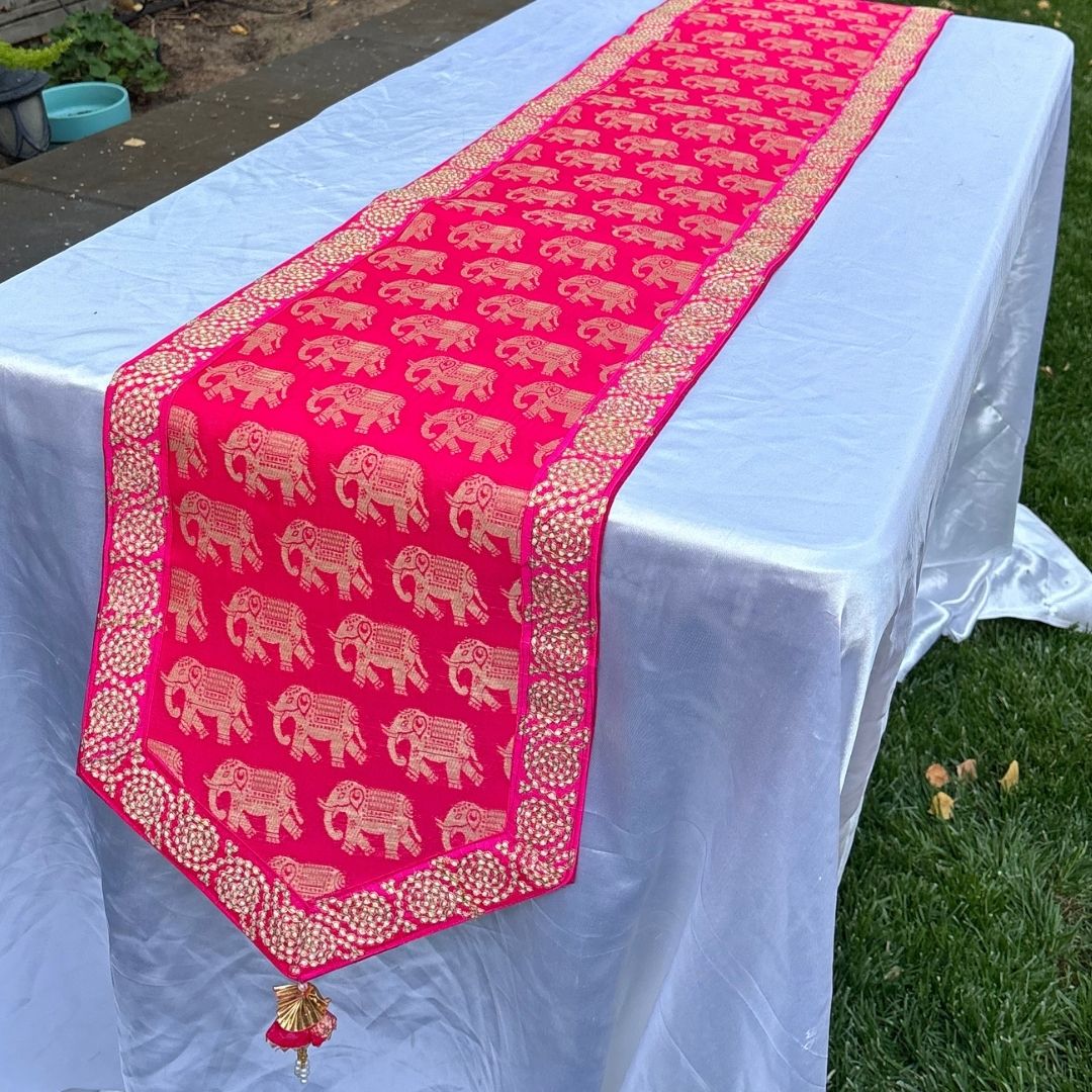 Pink table runner with elephant pattern on a white tablecloth outdoors.