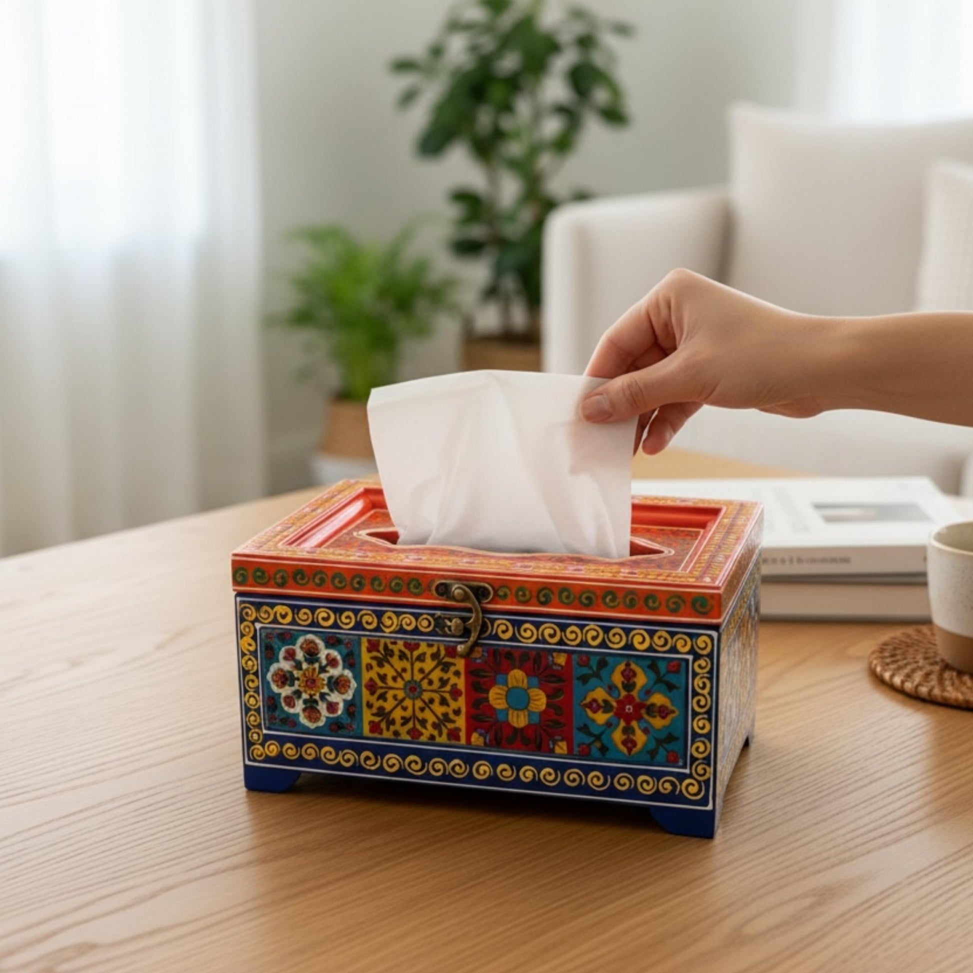 Hand pulling tissue from red and blue handpainted mango wood tissue box in bright living room