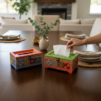Red and green handpainted mango wood tissue boxes on dark table, hand pulling tissue from green box
