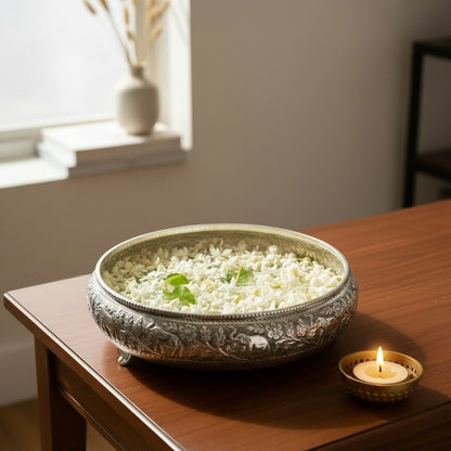Antique silver elephant urli bowl filled with jasmine beside a brass tealight holder on a wooden side table