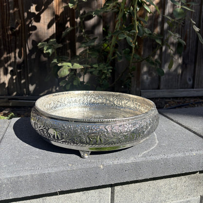 Side view of the antique silver urli bowl on its small feet, showing raised elephants and vines around the wall