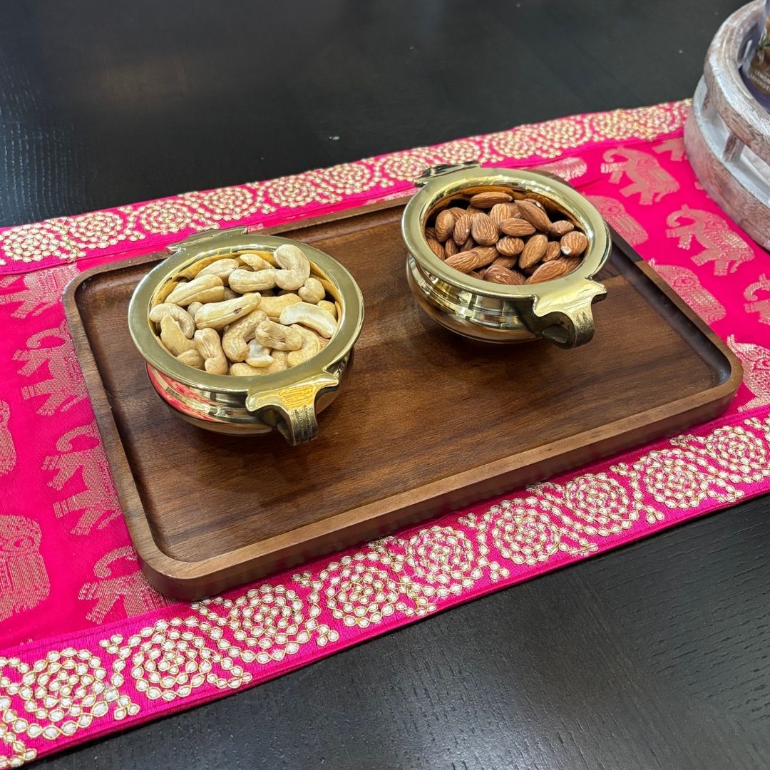 Brass urli bowls set filled with pink roses on a wooden tray – decorative Indian festivity decor