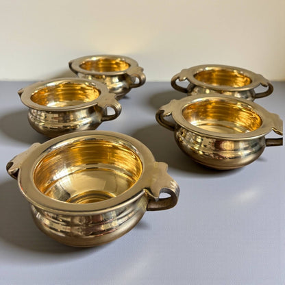 Five brass urli bowls with handles arranged on a light gray background – return gift favor set