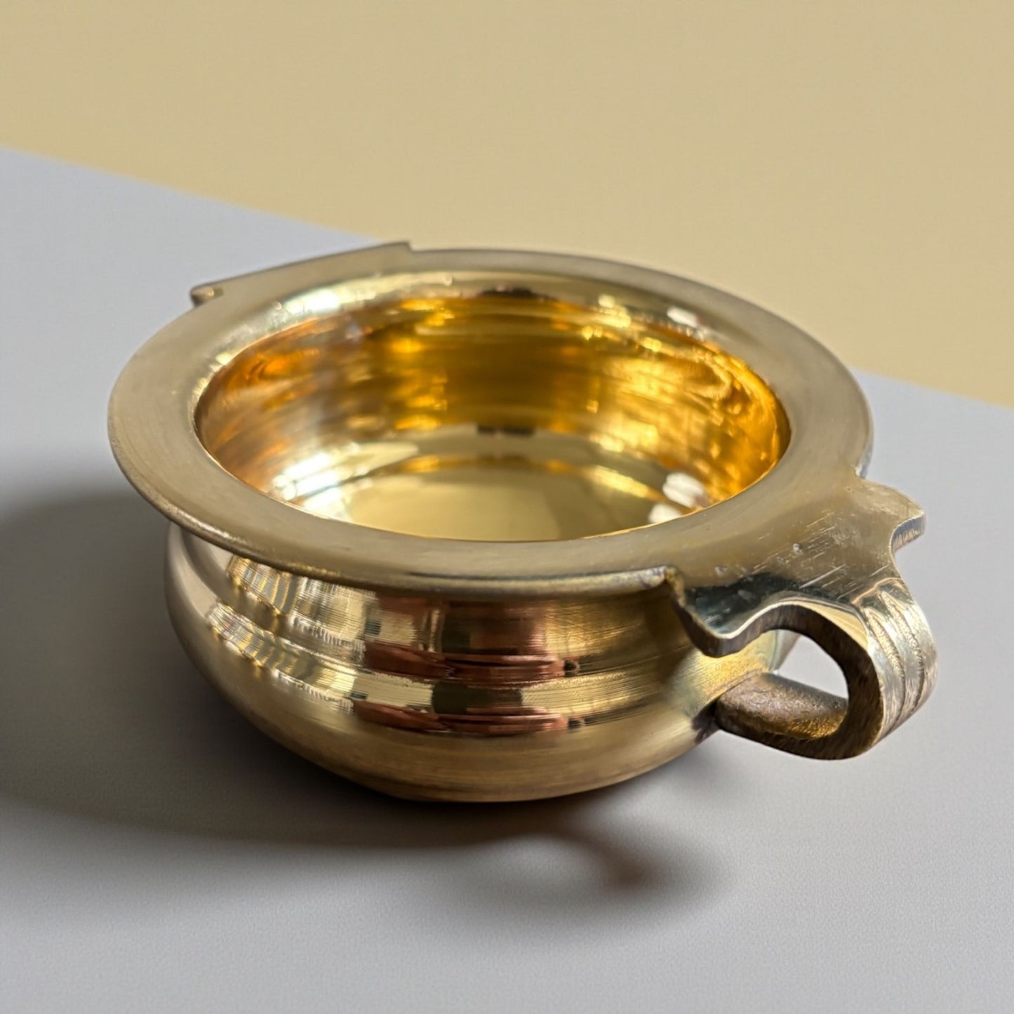 Close-up of a brass urli bowl with handles on a grey surface – handcrafted traditional design