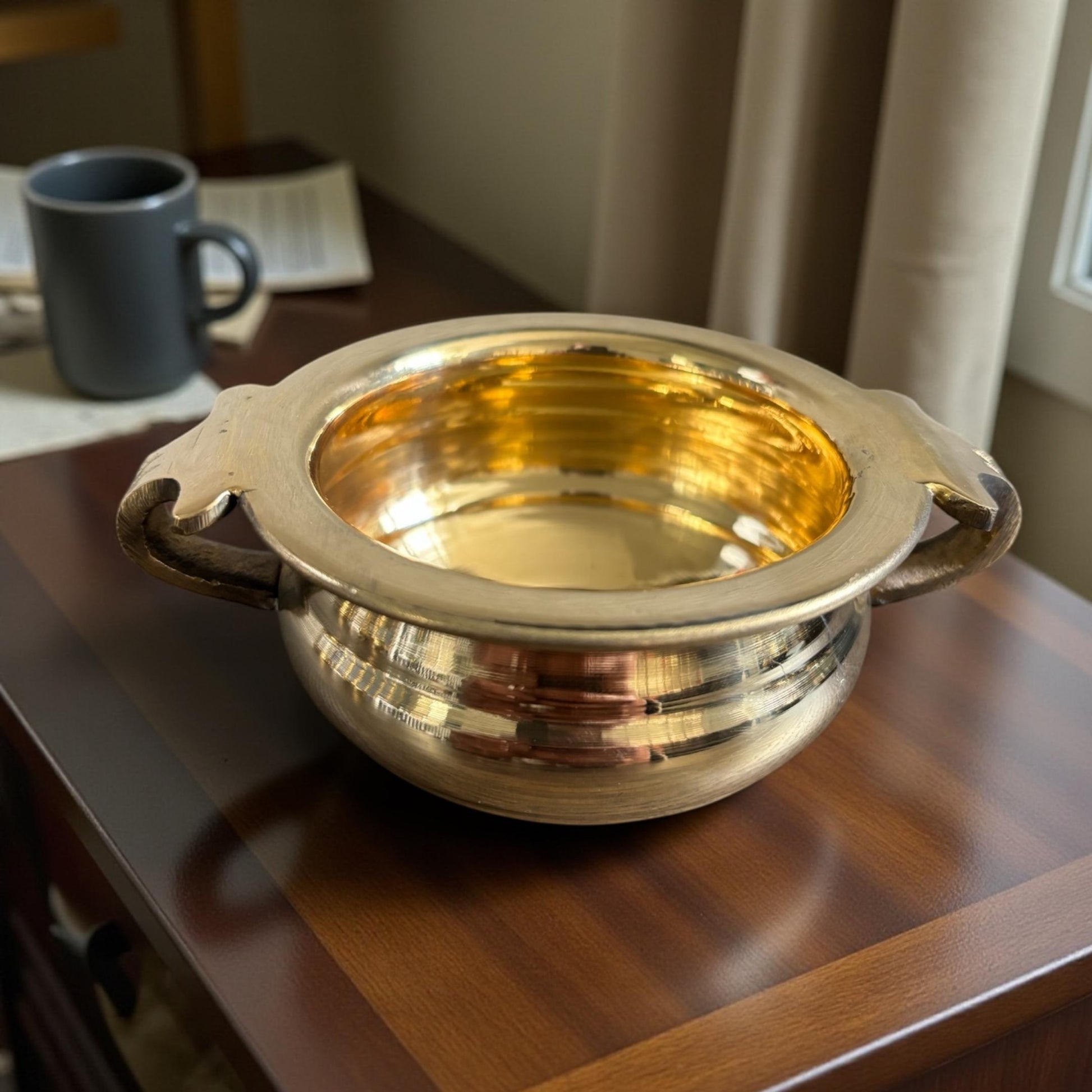 Brass urli bowl with decorative handles placed on a wooden table – home mandir or décor use