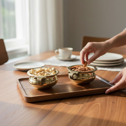 Two brass mini urli bowls holding nuts on wooden tray with patterned pink-gold mat – pooja serving idea