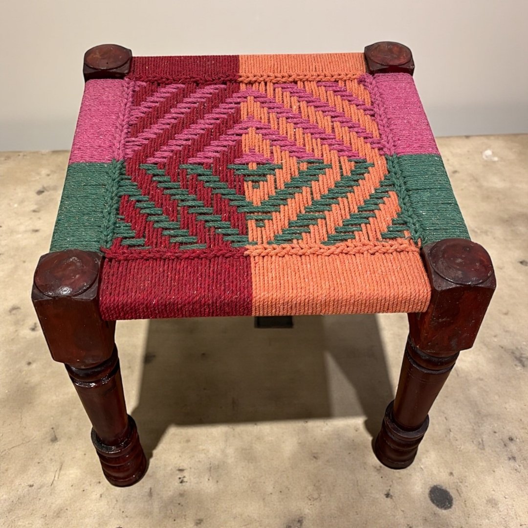 Small stool with a geometric patterned seat on a concrete floor.
