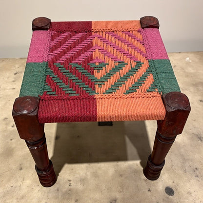 Small stool with a geometric patterned seat on a concrete floor.