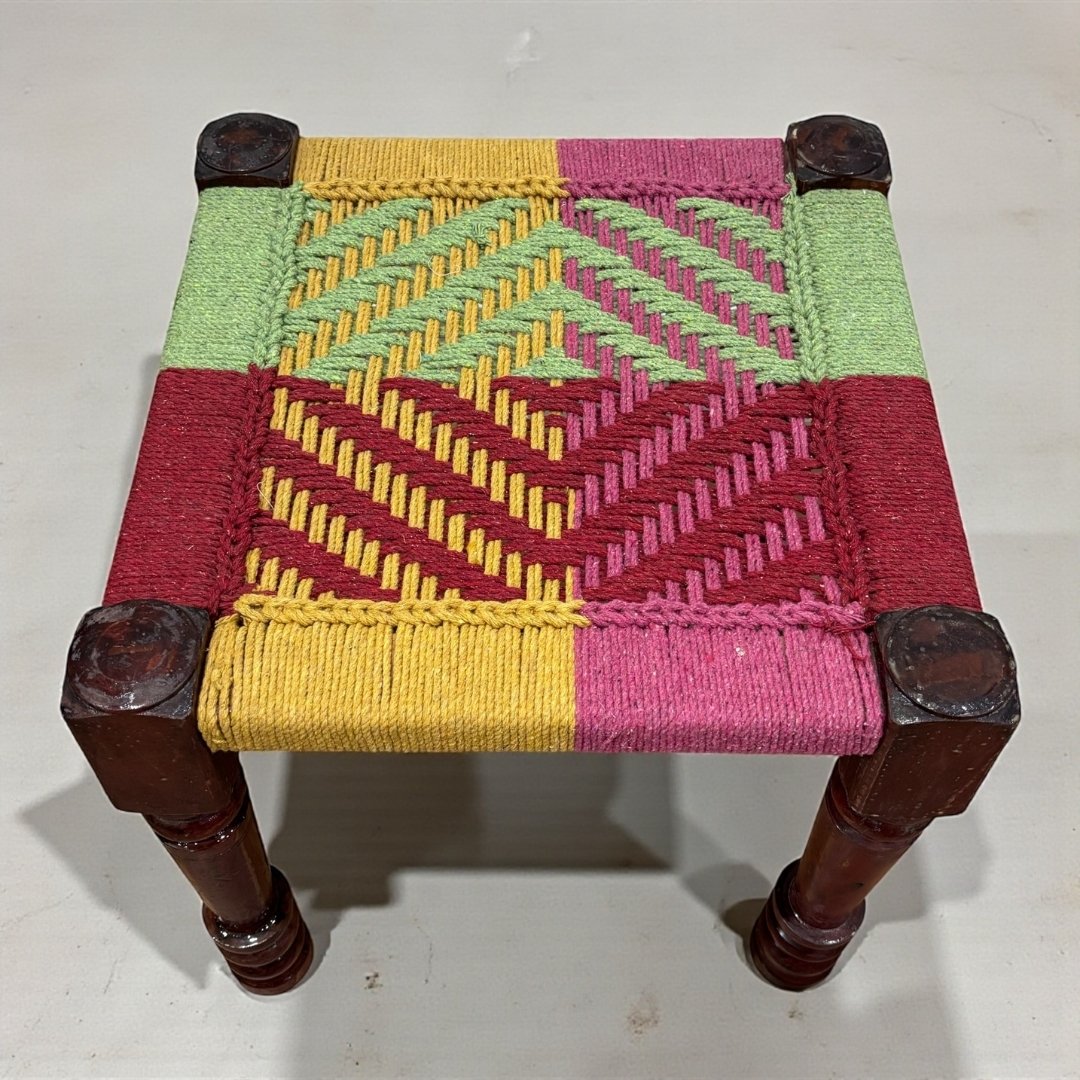 Small woven stool with colorful pattern on a white background