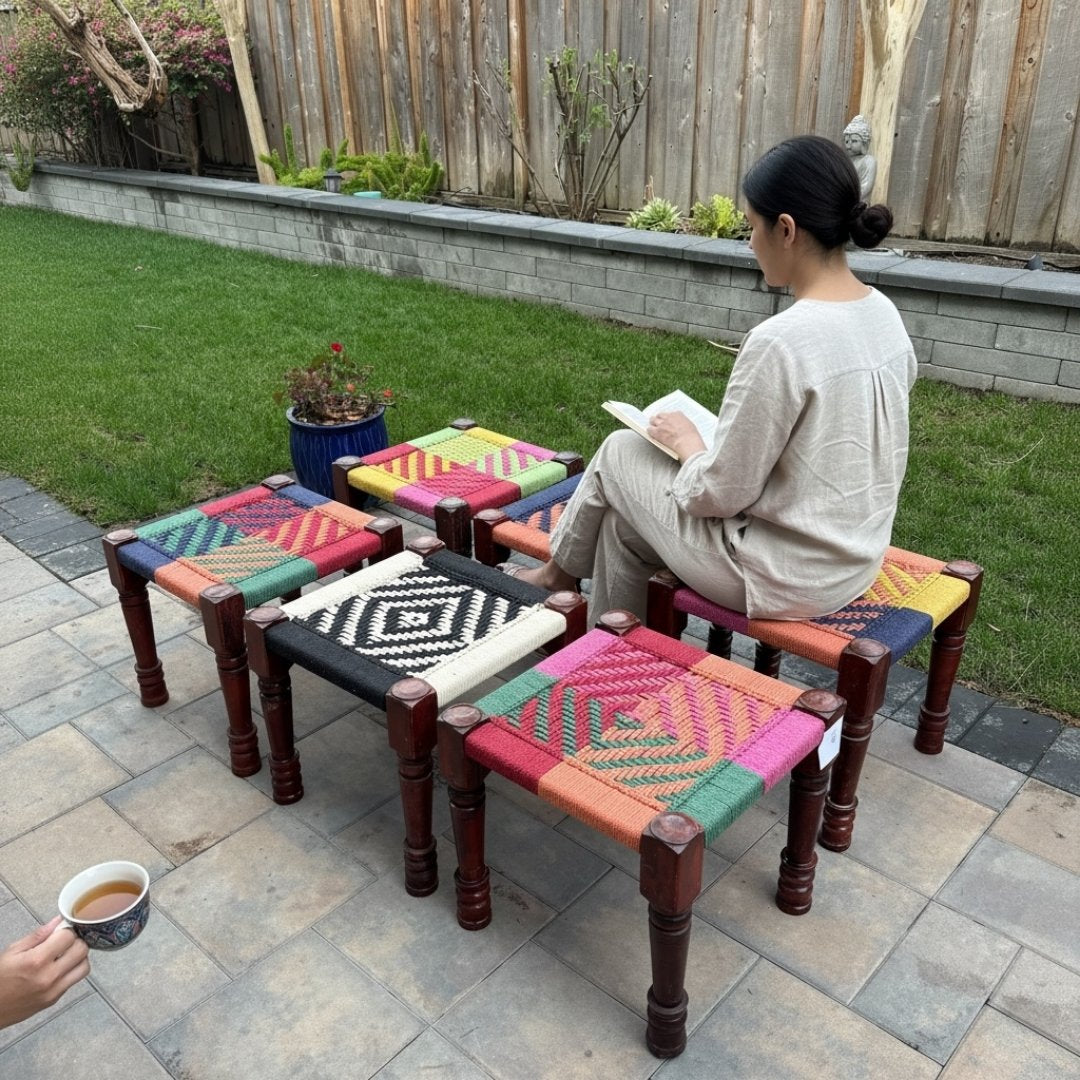 Woman sitting on a colorful woven stool from Urli Utsav Decor in a garden setting. 