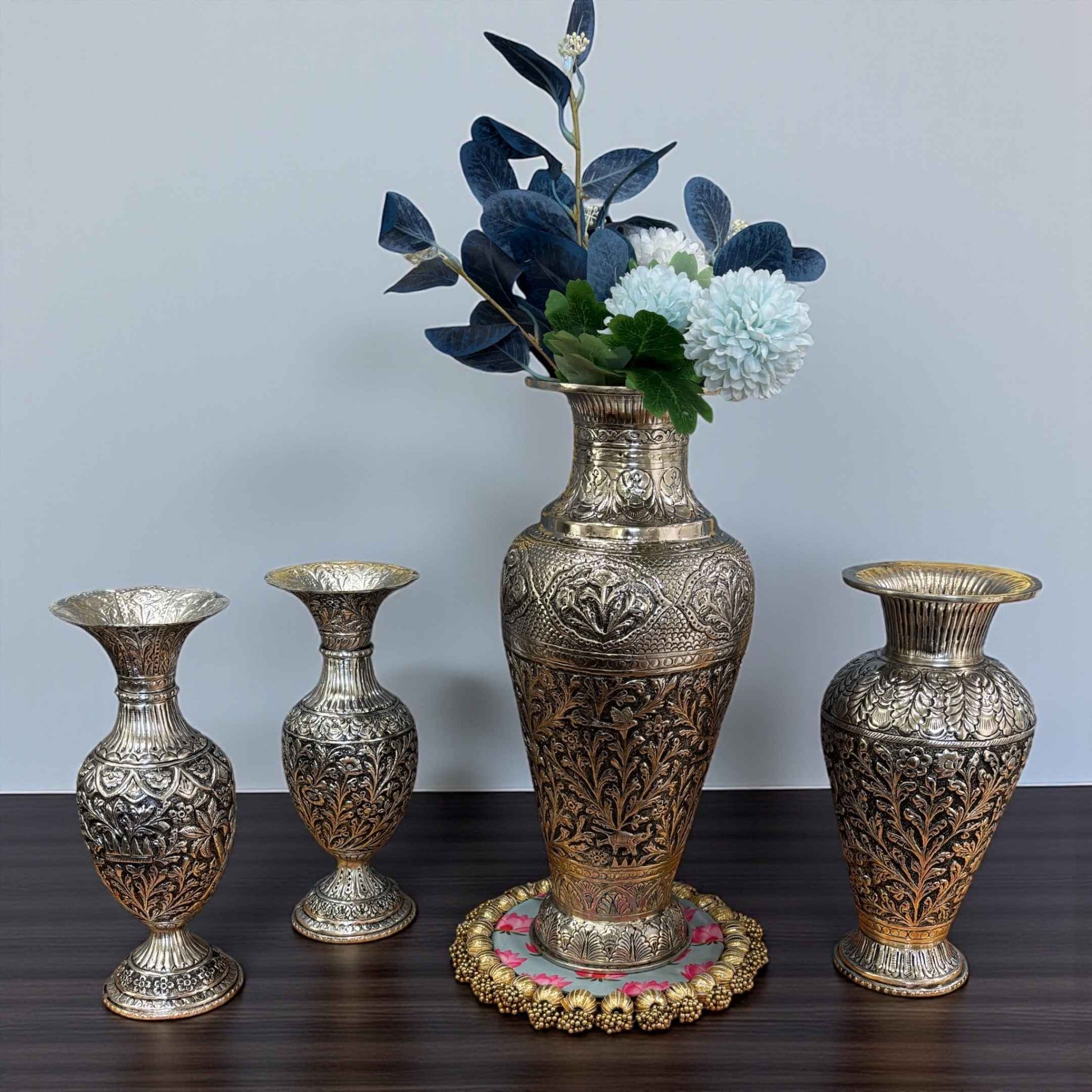 Set of ornate silver vases on a wooden surface with a plain background